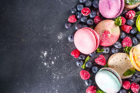 Colorful french macaron dessert. Set of various different tastes and color macaron cookies with berries, sugar powder and mint on dark grey stone backgroundの写真素材