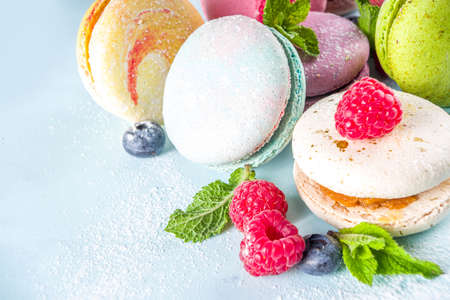 Colorful french macaron dessert. Set of various different tastes and color macaron cookies with berries, sugar powder and mint on blue backgroundの写真素材