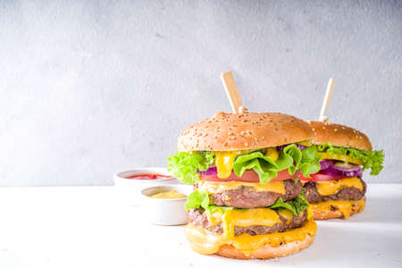 Tasty grilled homemade cheeseburgers with beef, tomato, cheese, tomato and lettuce. On white concrete background, with sauces. Top view copy spaceの写真素材