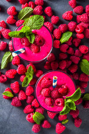Summer sweet diet appetizer. Raspberry fruit smoothie, milk shake in glass jars, top view. Berry healthy yogurt cocktail with fresh raspberries on dark grey backgroundの写真素材