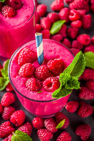 Summer sweet diet appetizer. Raspberry fruit smoothie, milk shake in glass jars, top view. Berry healthy yogurt cocktail with fresh raspberries on dark grey backgroundの写真素材