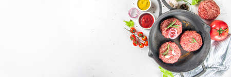 Cooking burger background. Set various cheeseburger and beefburger ingredients - bun, tomatoes, onion, lettuce, sauces, cheese and raw burger cutlets, ready for barbecue grill. Burger bbq party fest concept, top view copy spaceの写真素材