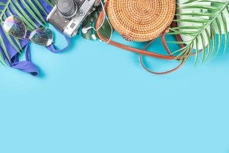 Summer vacation and travel concept. Beach accessories things - bag, hat, swimsuit, sunglasses, camera, tropical leaves on aquamarine, turquoise blue backdrop. Summer is coming trendy conceptの写真素材