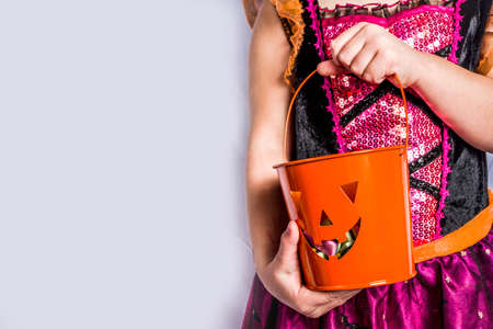 Little cute girl in witch costume for Halloween with jack-o-lantern bucket for Halloween trick or treating. White wall background copy spaceの写真素材