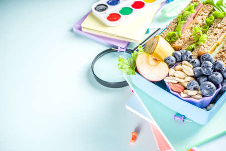 Healthy children school lunch box: sandwich, vegetables, fruit and mineral water bottle, with school supplies on, on light blue background copy spaceの写真素材