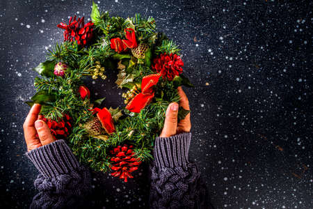 Christmas wreath with fir branches, berries, pine cones, and thread. Girl hands in pics, hold Christmas wreathの写真素材