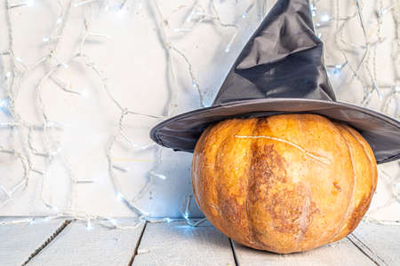 Pumpkins with witch black hat on white wooden background, with white festive garland over wall copy space. Halloween conceptの写真素材