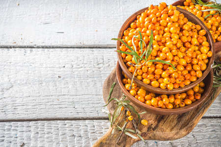 Sea buckthorn berries in small organic wooden bowl, with sea buckthorn branches on white wooden desk...