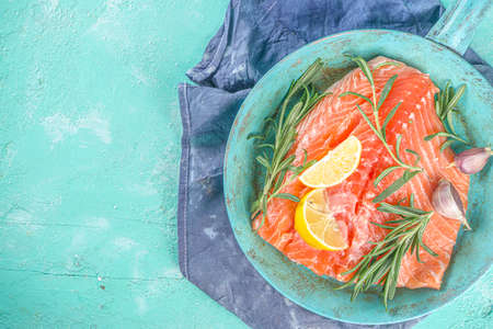 Salmon. Fresh raw salmon fish fillet with cooking ingredients, herbs and lemon in cooking pan, skillet, light blue Turquoise background, top viewの写真素材