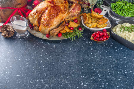 Christmas or New Year turkey dinner. Baked turkey with potato, red berries and sage leaves, on Christmas dinner table with Xmas tree, gift and candles backgroundの写真素材