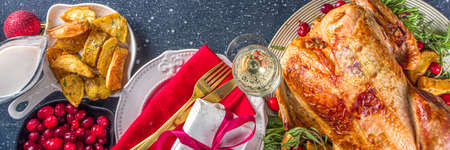 Christmas or New Year turkey dinner. Baked turkey with potato, red berries and sage leaves, on Christmas dinner table with Xmas tree, gift and candles backgroundの写真素材