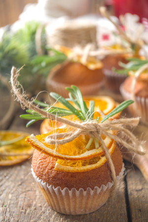 Winter christmas homemade baking recipe. Spicy muffins, orange cupcakes, citrus zest, rosemary and spices. On a wooden background with branches of a Christmas treeの写真素材