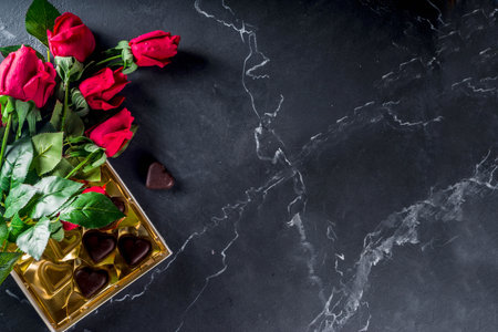Valentines day with red roses and chocolate hearts on black marble stone background. Top view with spaceの写真素材