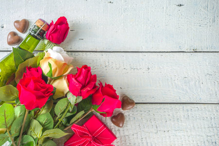 Valentines day greeting card concept with red rose flowers, champagne, chocolates and gift box. Top view flat lay on white wooden background with space for greetingsの写真素材