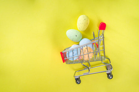 Easter sale concept, spring update collection. Easter colorful painted eggs in a shopping cart on bright yellow background top view copy spaceの写真素材