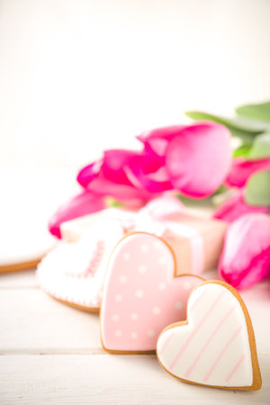 Valentine Day concept, Spring Woman Day Holiday, Mothers Day background, Red tulip flowers bouquet, craft paper gift box, heart shaped traditional sugar cookies, White wooden background copy spaceの写真素材