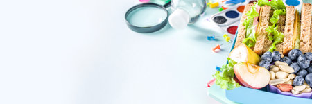 Healthy children school lunch box: sandwich, vegetables, fruit and mineral water bottle, with school supplies on, on light blue background copy spaceの写真素材