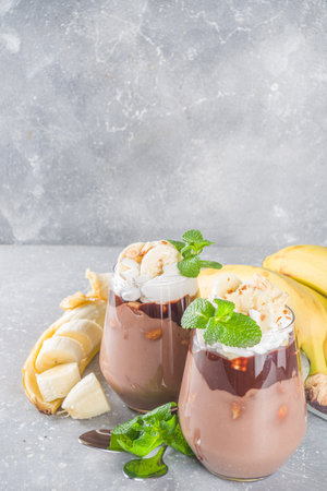 Chocolate banana pudding, layered dessert in glass with banana slices and chocolate topping. Delicious vegan chocolate mousse with banana, cocoa and nuts, gray stone background copy spaceの写真素材