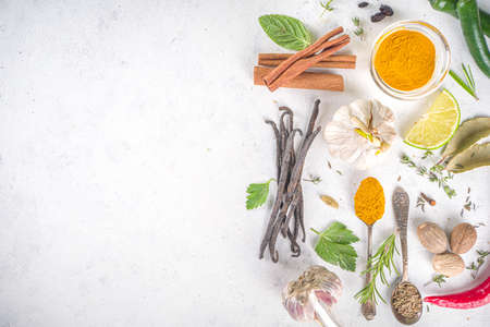 Fresh herbs, dried colorful spices. Cooking background flatlay with variety spices, herbs pepper, vanilla bean, cinnamon, basil, rosemary, chilli red green peppers, mint, parsley White table top viewの写真素材