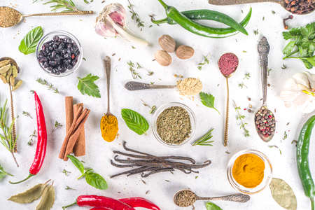 Fresh herbs, dried colorful spices. Cooking background flatlay with variety spices, herbs pepper, vanilla bean, cinnamon, basil, rosemary, chilli red green peppers, mint, parsley White table top viewの写真素材