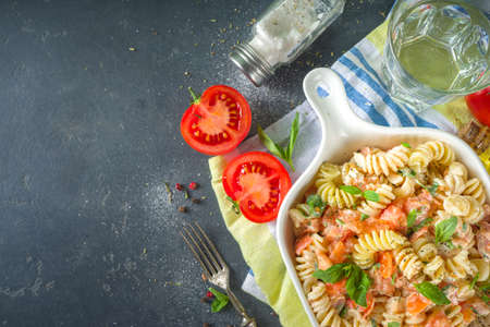 Spring diet healthy vegan pasta. Italian fusilli pasta with tomatoes, green vegetables, fresh herbs, cream cheese or feta, on dark table background copy spaceの写真素材