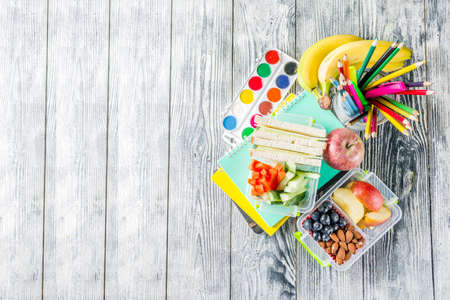Healthy school lunch box. Kid's lunch box with sandwiches, fruit, vegetables, nuts, water and school supplies, White wooden backgroundの写真素材