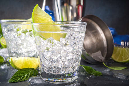 Summer paloma cocktail, vodka lime, mojito or gin tonic with lime wedge and crushed ice in rocks, two cold alcohol beverage glasses on black background copy spaceの写真素材