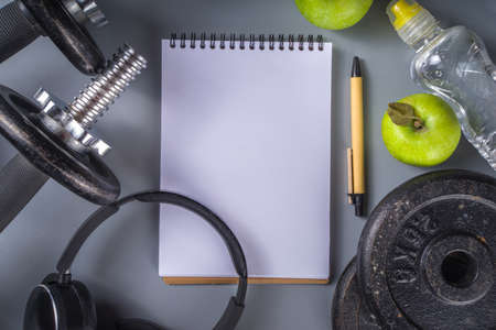 Mens Fitness background with dark Iron dumbbells, sneakers, headphones, gren apples and water bottle. On gray background top view copy spaceの写真素材