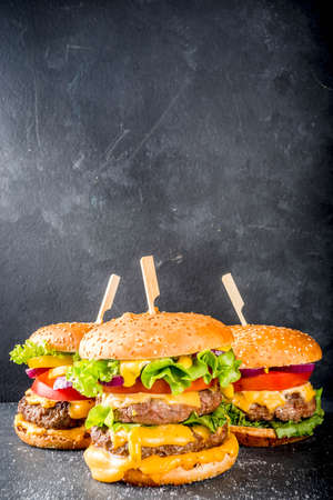 Tasty grilled homemade cheeseburgers with beef, tomato, cheese, tomato and lettuce. On dark gray background, with sauces. Top view copy space