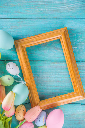 Spring and Easter holiday background with tulip flowers, colorful pastel eggs on blue table top...