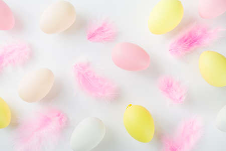 Pastel colored flatlay with Easter colored eggs and feathers on white table. Easter simple pattern background, spring holidays conceptの写真素材
