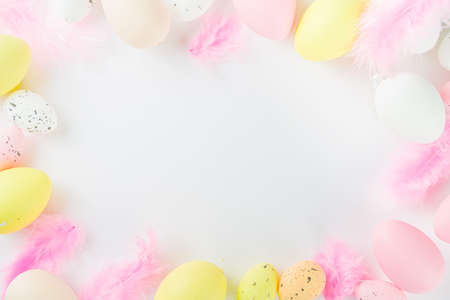 Pastel colored flatlay with Easter colored eggs and feathers on white table. Easter simple pattern...