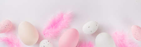 Pastel colored flatlay with Easter colored eggs and feathers on white table. Easter simple pattern background, spring holidays conceptの写真素材