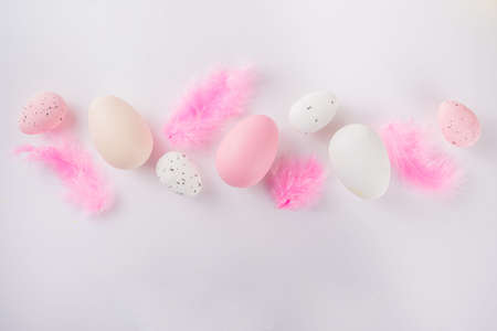 Pastel colored flatlay with Easter colored eggs and feathers on white table. Easter simple pattern background, spring holidays conceptの写真素材