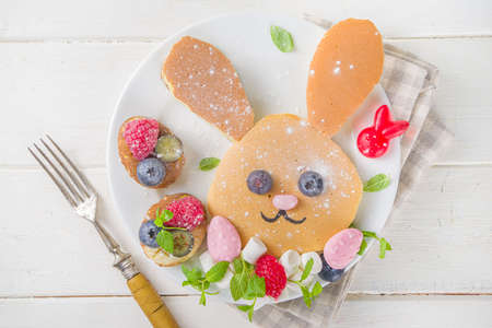 Funny bunny pancakes, Cute Kids Breakfast for Easter morning. Creative rabbits pancakes with fresh berry decoration, top view on white wooden background copy spaceの写真素材