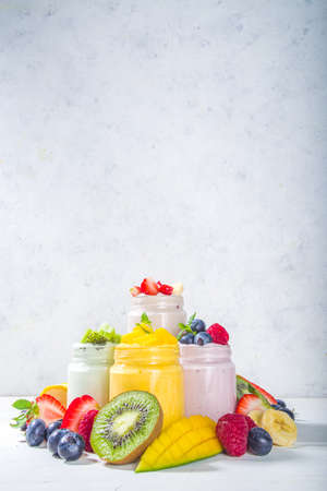Set of various fruit and berry sweet yogurts in glass jars. Variety healthy Breakfast yoghurt with blueberry, strawberry, mango, kiwi, raspberry, with fresh fruits and berries, white wooden backgroundの写真素材