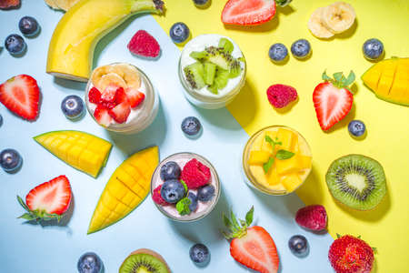 Set of various fruit and berry yogurts in glass jars. Variety healthy Breakfast yoghurt with blueberry, strawberry, mango, kiwi, raspberry, trendy bright yellow background with hard light dark shadowsの写真素材