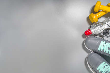 Woman athlete's set with dumbbells and bottle of water headphones. Sport and fitness concept on gray...