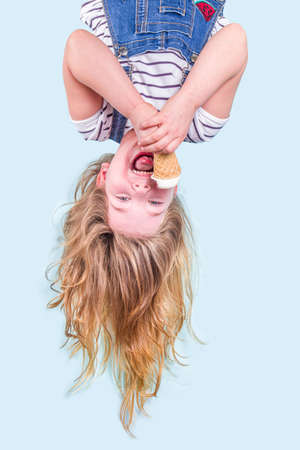Cute joyful happy toddler child girl upside down with fluttering hair, eating vanilla ice cream. Summer vacation fun concept on blue background copy spaceの写真素材