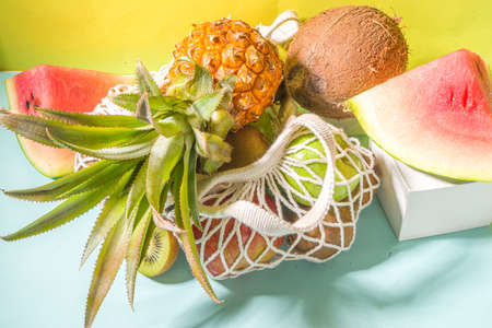 Summer fruit shopping background. Eco-friendly shopping bag full of fresh tropical fruits, on modern bright background with hard light copy space. Vitamin, healthy diet food conceptの写真素材