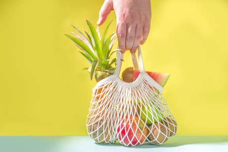 Summer fruit shopping background. Eco-friendly shopping bag full of fresh tropical fruits, on modern bright background with hard light copy space. Vitamin, healthy diet food conceptの写真素材