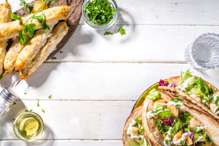 Mediterranean food. Doner Kebap, Taco, Shawarma, greek wrapped gyros sandwich, tortilla pita bread stuffed grilled chicken meat, fresh vegetables, tsatziki sauce. Sunny white wooden table copy spaceの写真素材