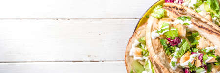 Mediterranean food. Doner Kebap, Taco, Shawarma, greek wrapped gyros sandwich, tortilla pita bread stuffed grilled chicken meat, fresh vegetables, tsatziki sauce. Sunny white wooden table copy spaceの写真素材