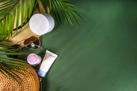 Blank white and pastel colored cosmetic bottles mock up, on green background with a tropical leaves,...