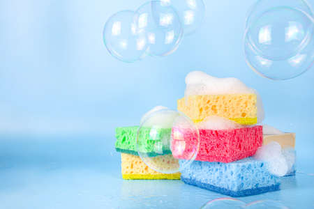 Spring home cleaning, housekeeping concept, Set of various bright detergent washing rubber sponges for cleaning, with lush foam and soap bubbles on a blue background top view copy spaceの写真素材