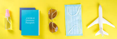 Toy airplane, tropical vacation decor and accessories, face medical mask, antiseptic spray on yellow bright background. Travel during concept.  immunization passport cardの写真素材