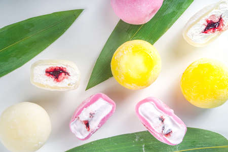 Traditional Japanese dessert mochi. Colorful mochi ice cream on a white table, whole and cut with berry, fruit fillingの写真素材