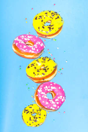 Flying donuts. Pink and yellow donuts with sprinkles on blue background