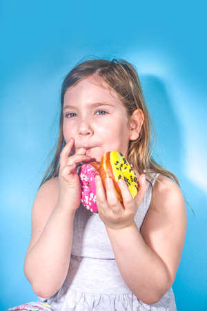 Little happy funny girl with colorful sugar glazed pink and yellow donuts, Holiday, happiness,...