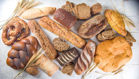 Assortment of various delicious freshly baked bread, on white background top view copy space